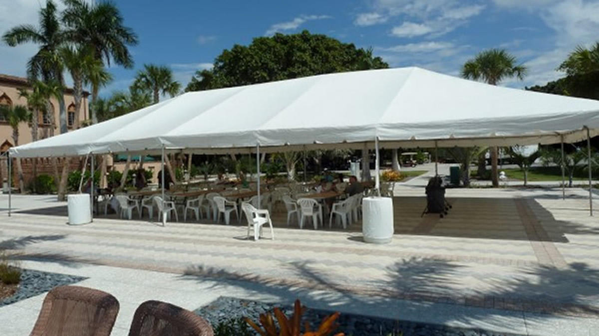 White frame tent with tables set up under palm trees for an evening event