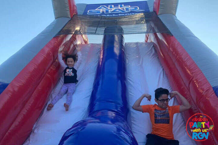 Two kids cheering at the bottom of a tall red and blue inflatable slide