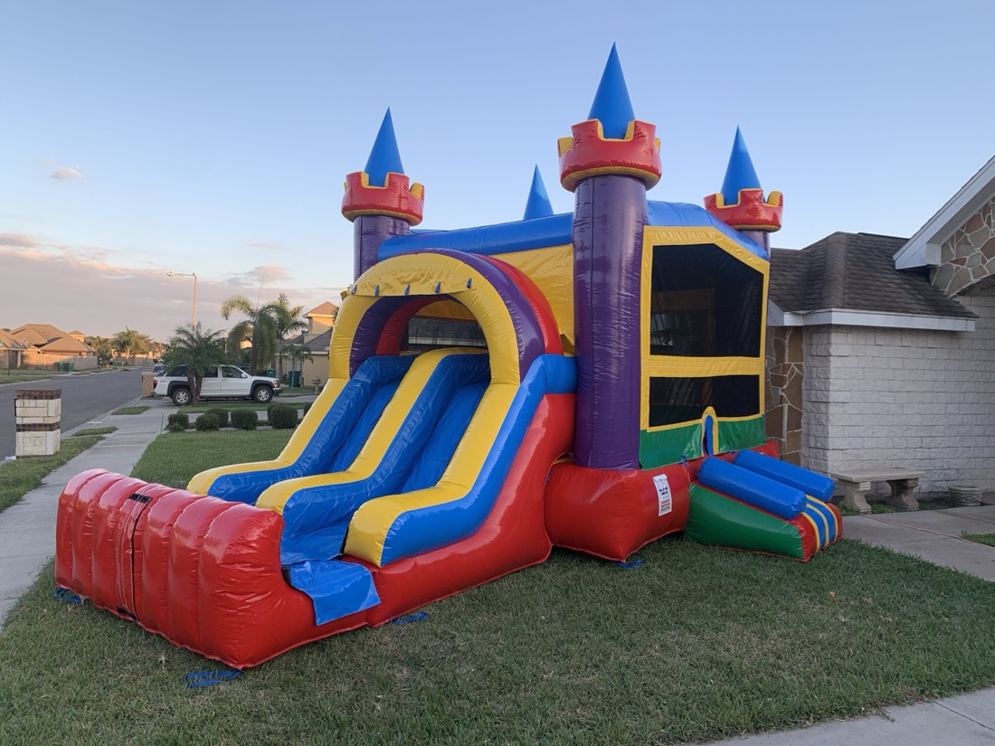 Bright red, yellow and blue castle bounce house with a double slide set up in a Valley backyard